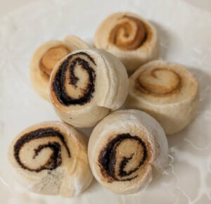 Rolled cookies (small Swiss rolls) sliced into rounds with chocolate and jam filling on a plate, lightly dusted with sugar sugar.